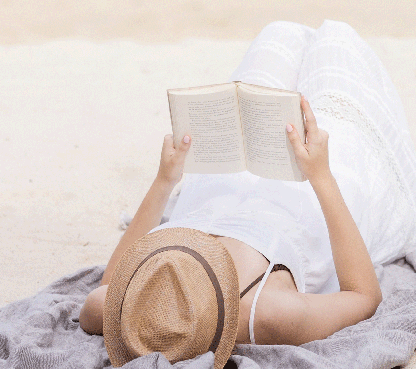 Frau von hinten mit Strohhut am Strand mit einem Buch in der Hand. Pastell Farben. Beige, hellblau und braun. Entspannte Szene